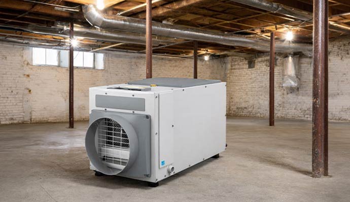 Commercial dehumidifier unit installed on concrete floor in an unfinished basement