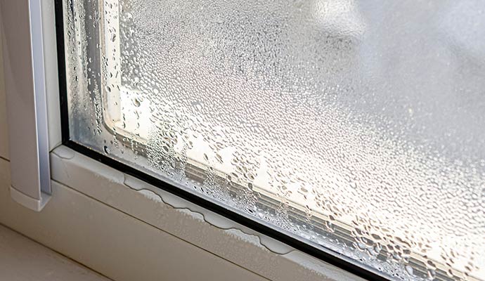 A close-up view of heavy condensation and water droplets on the interior surface of a glass window pane